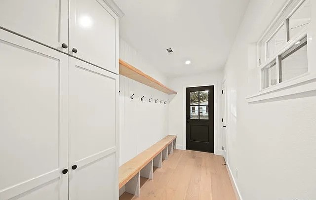 Bright mudroom with white shaker cabinetry, wood bench and black entry door