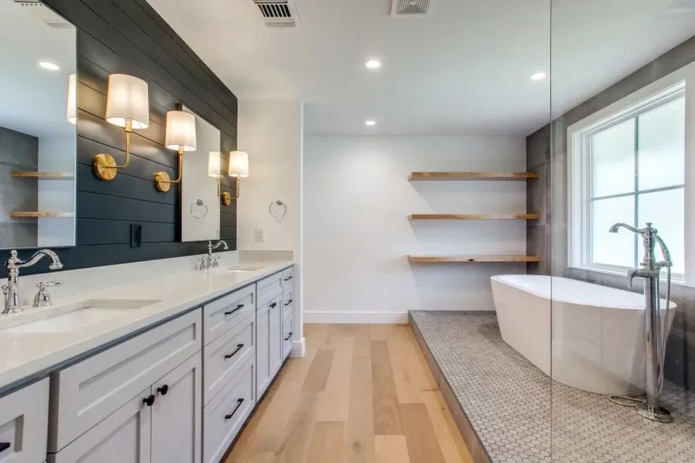 Master bath with dark shiplap accent wall, double vanity, freestanding tub and gold sconces