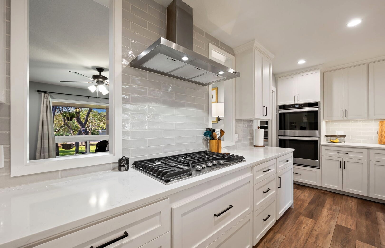 White kitchen with gas cooktop, subway tile backsplash and stainless range hood