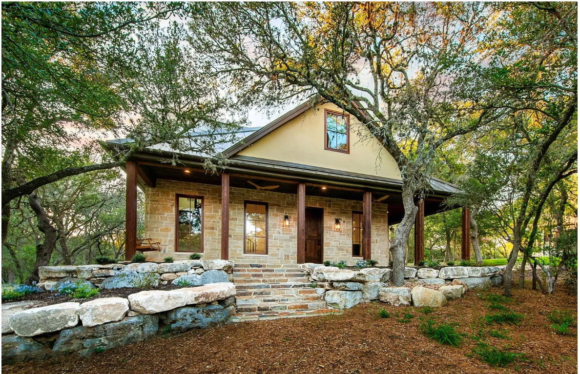 Stone cottage with covered porch nestled among live oaks
