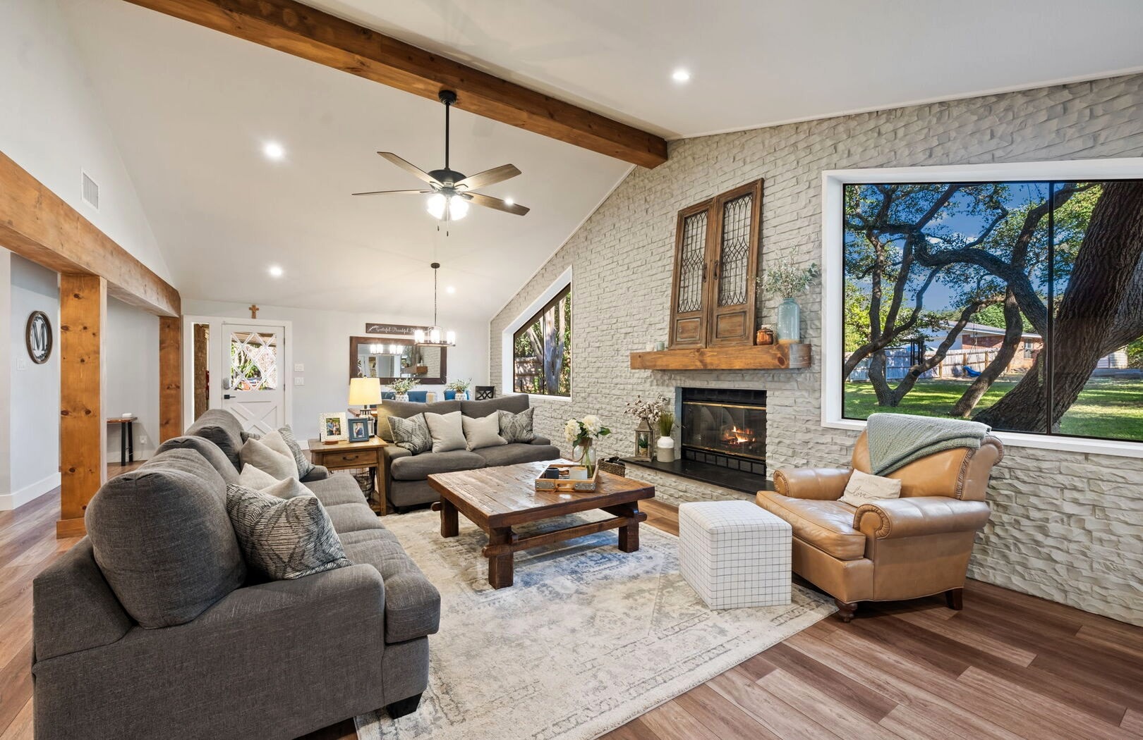 Vaulted living room with white stone fireplace, wood beams and oak tree view