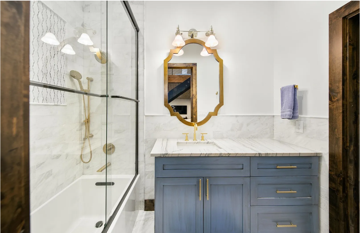 Bathroom with blue vanity, gold mirror and marble tile